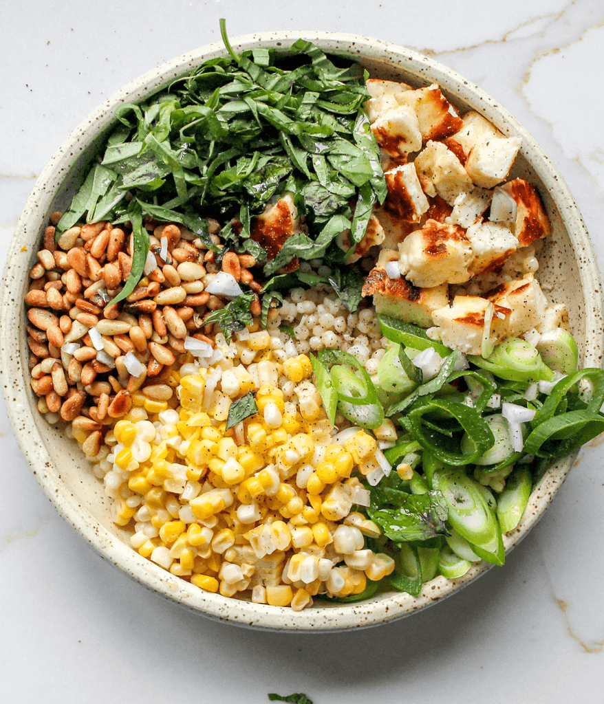 All ingredients for a pearl couscous salad scooped into bowl
