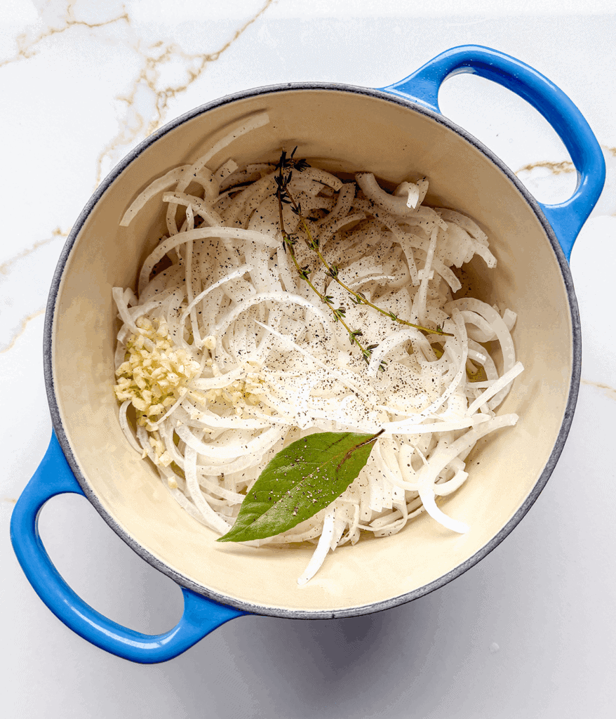 Onions, garlic, herbs, and bay leaf in a pot for French onion soup.