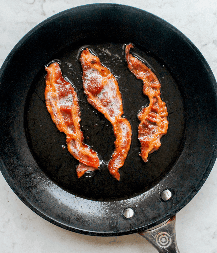 cooking bacon in a pan for an Avocado BLT