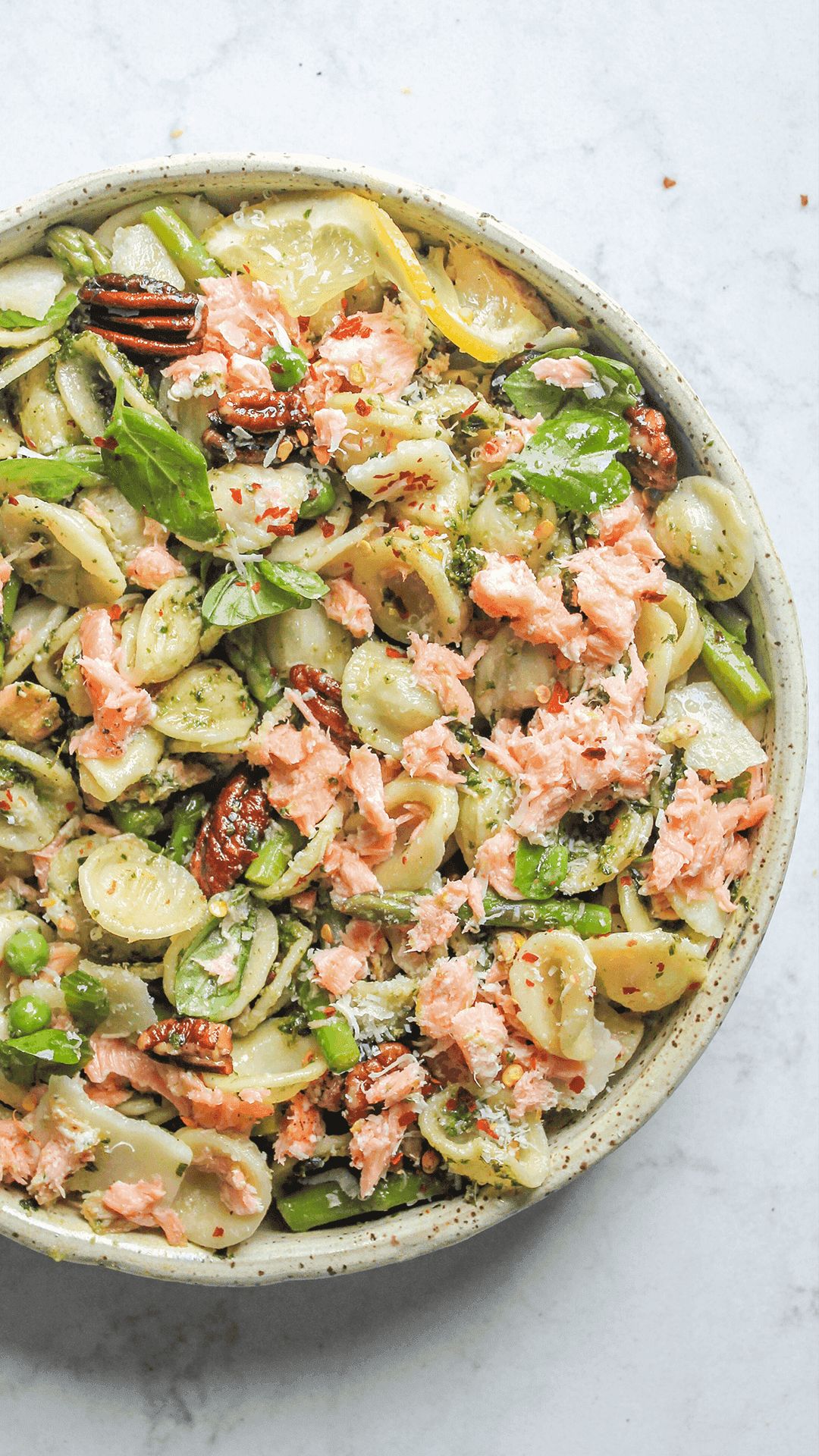 close up of salmon pesto pasta in a tan bowl.