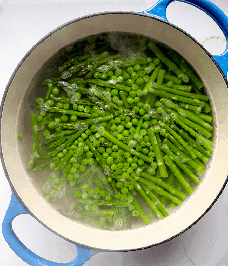 A blue pot with peas and asparagus boiling.
