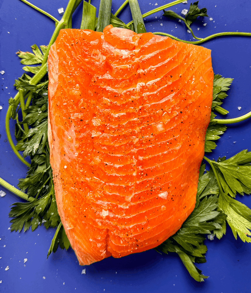 salmon over herbs on a baking sheet ready to be baked. 